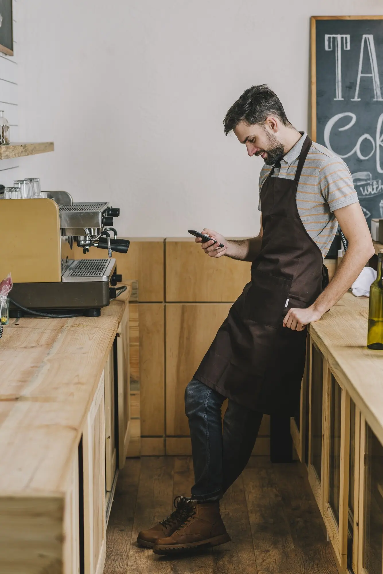Lächelnder Barista, der ein Smartphone nutzt.