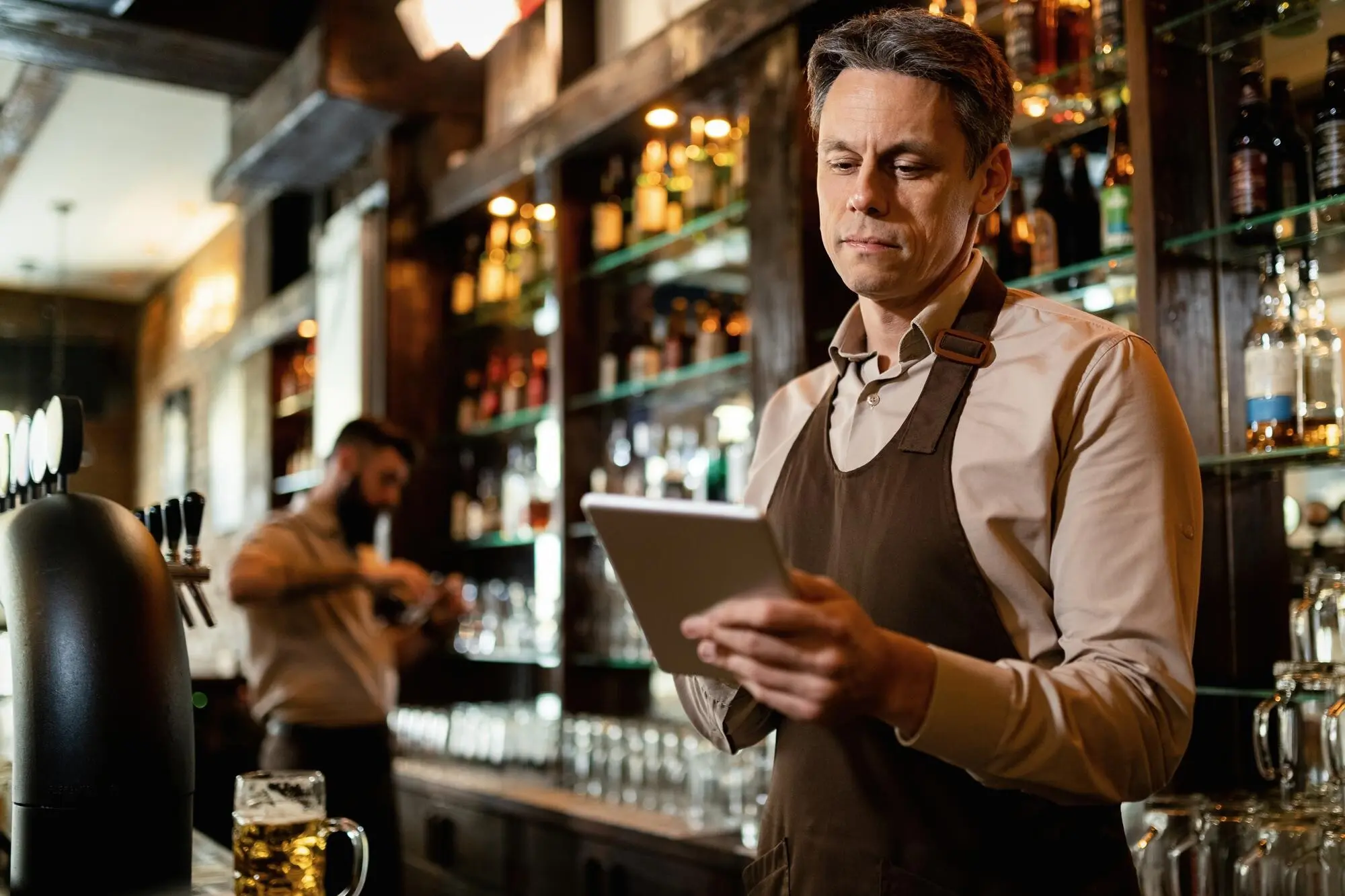 Lächelnder Kellner mittleren Alters, der bei der Arbeit in einer Bar ein Touchpad benutzt.