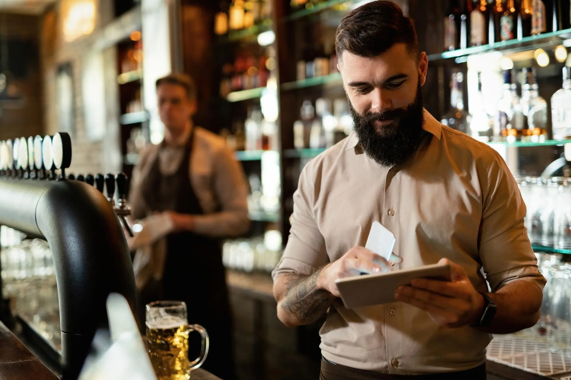 Ein junger, glücklicher Barista arbeitet in einer Bar und surft auf einem Touchpad im Internet.